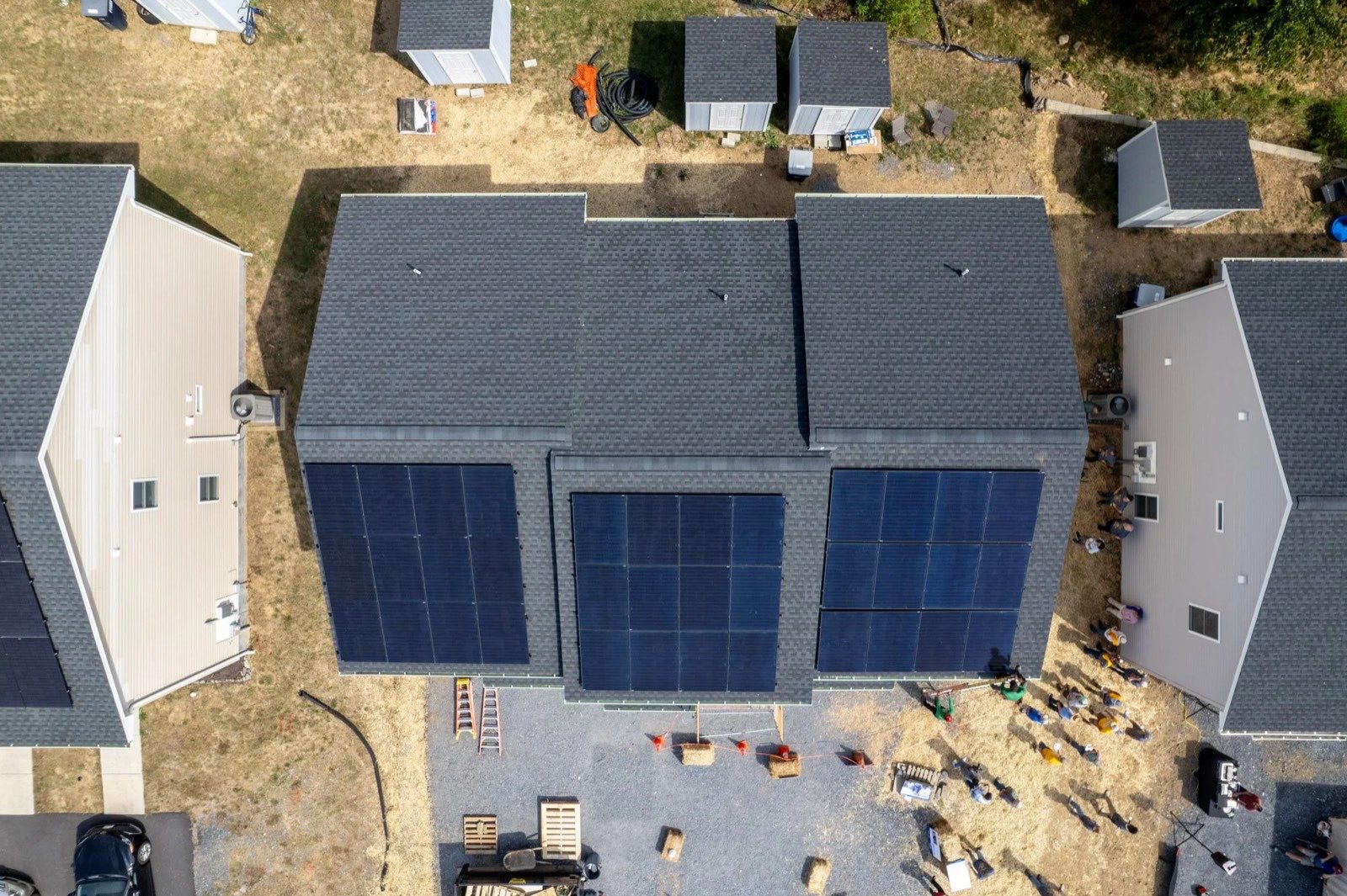 Two newly built Habitat homes seen from above, rooftop arrays freshly installed, tools still staged below.