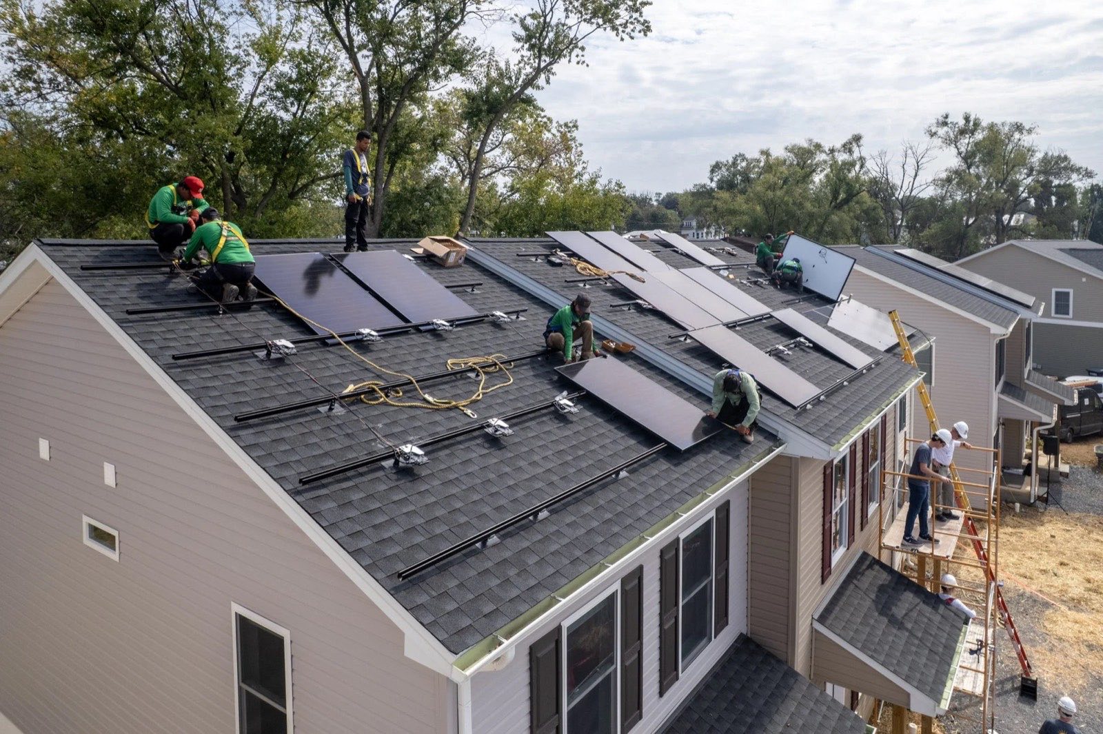 A volunteer crew spread across the roof of a Habitat home, fixing rails and panels in place.